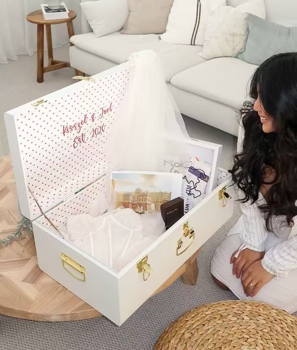 Woman sitting next to a white jewelry box with gold accents in a living room.