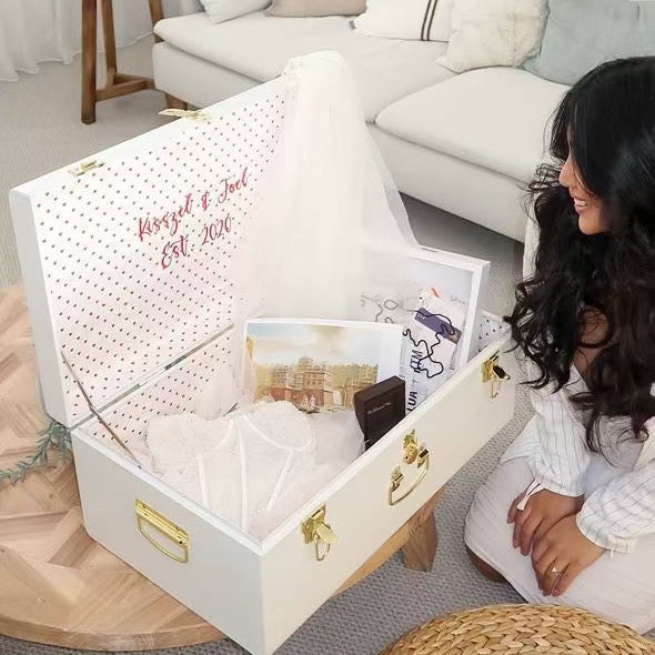 Woman sitting next to a white jewelry box with gold accents in a living room.