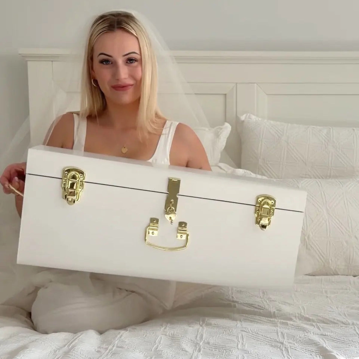 Woman holding a white suitcase with gold locks on a bed.