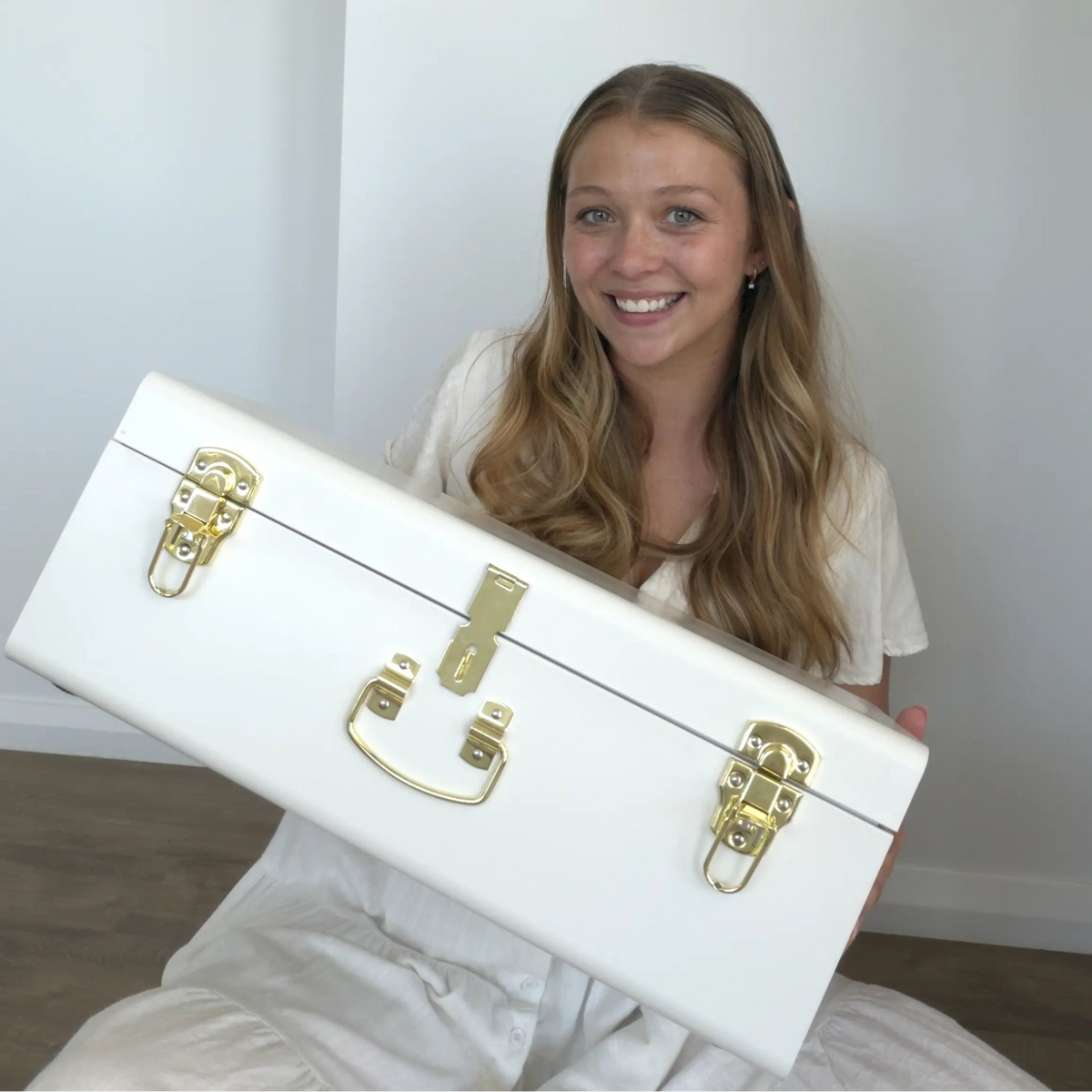 Woman holding a white suitcase with gold hardware against a plain background