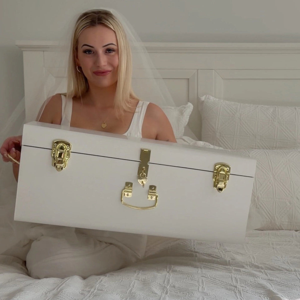Woman holding a white suitcase with gold locks in a bedroom setting