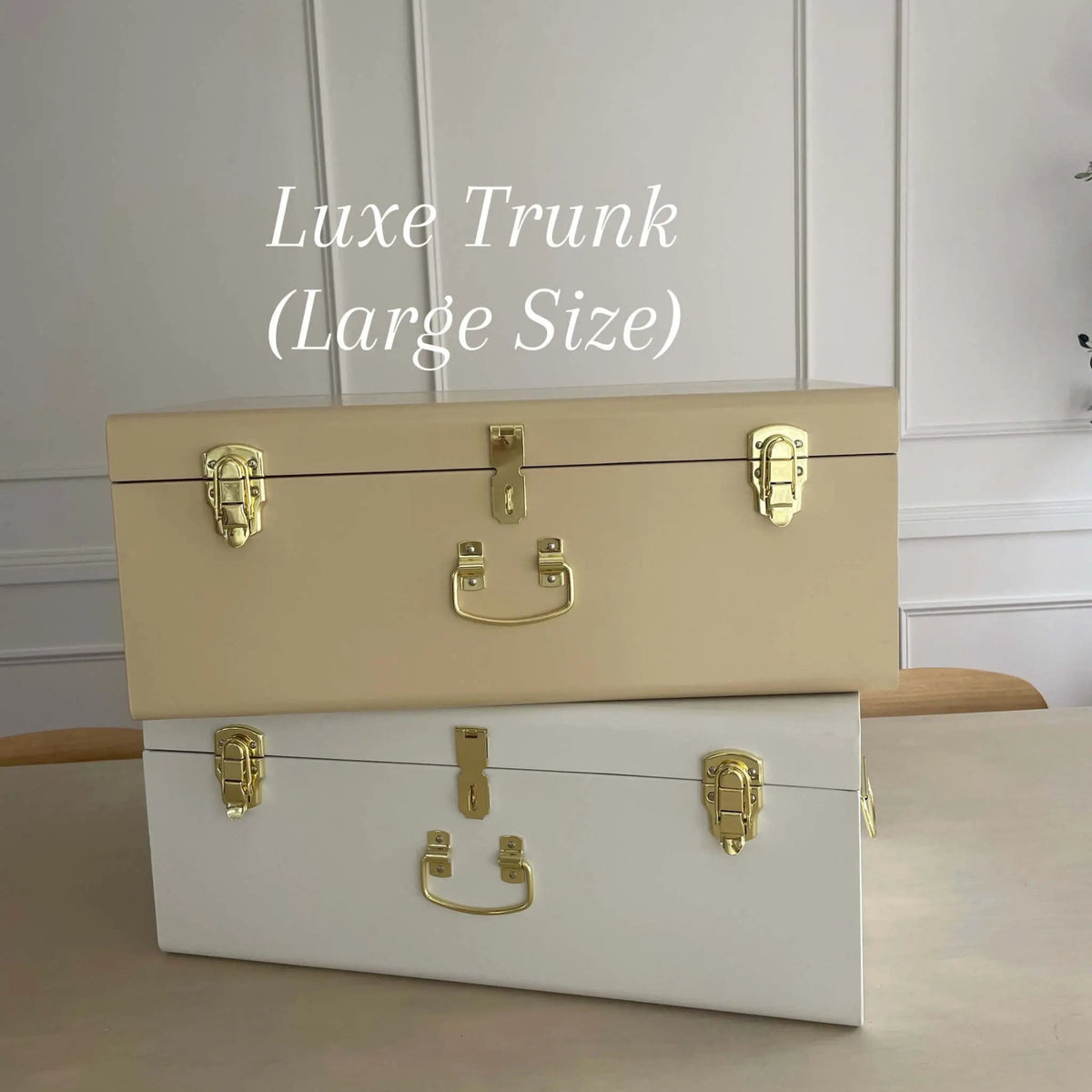 Two trunks, one beige and one white, with gold hardware on a wooden surface.