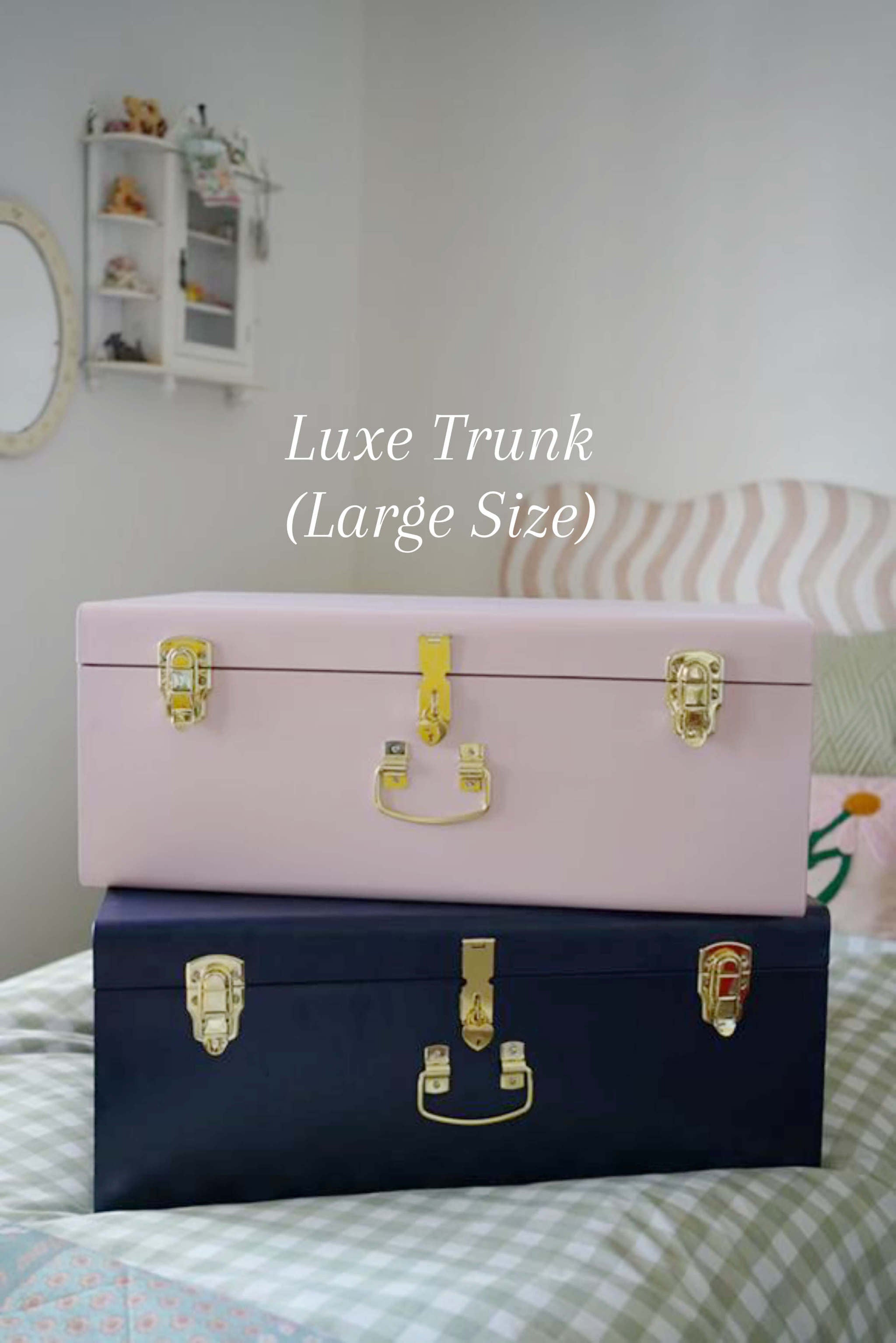 Two trunks, one pink and one navy, with gold latches on a bed.
