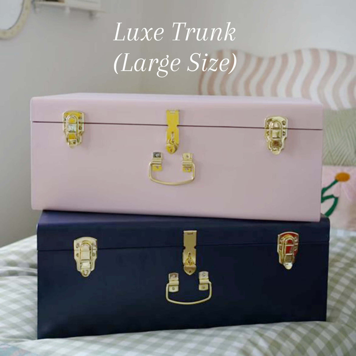 Two trunks, one pink and one navy, with gold latches on a bed.