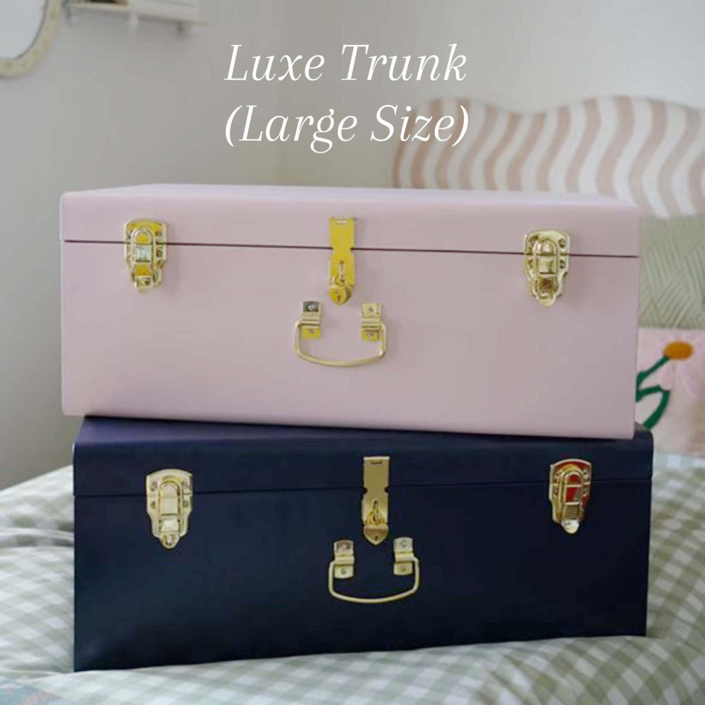 Two trunks, one pink and one navy, with gold latches on a bed.