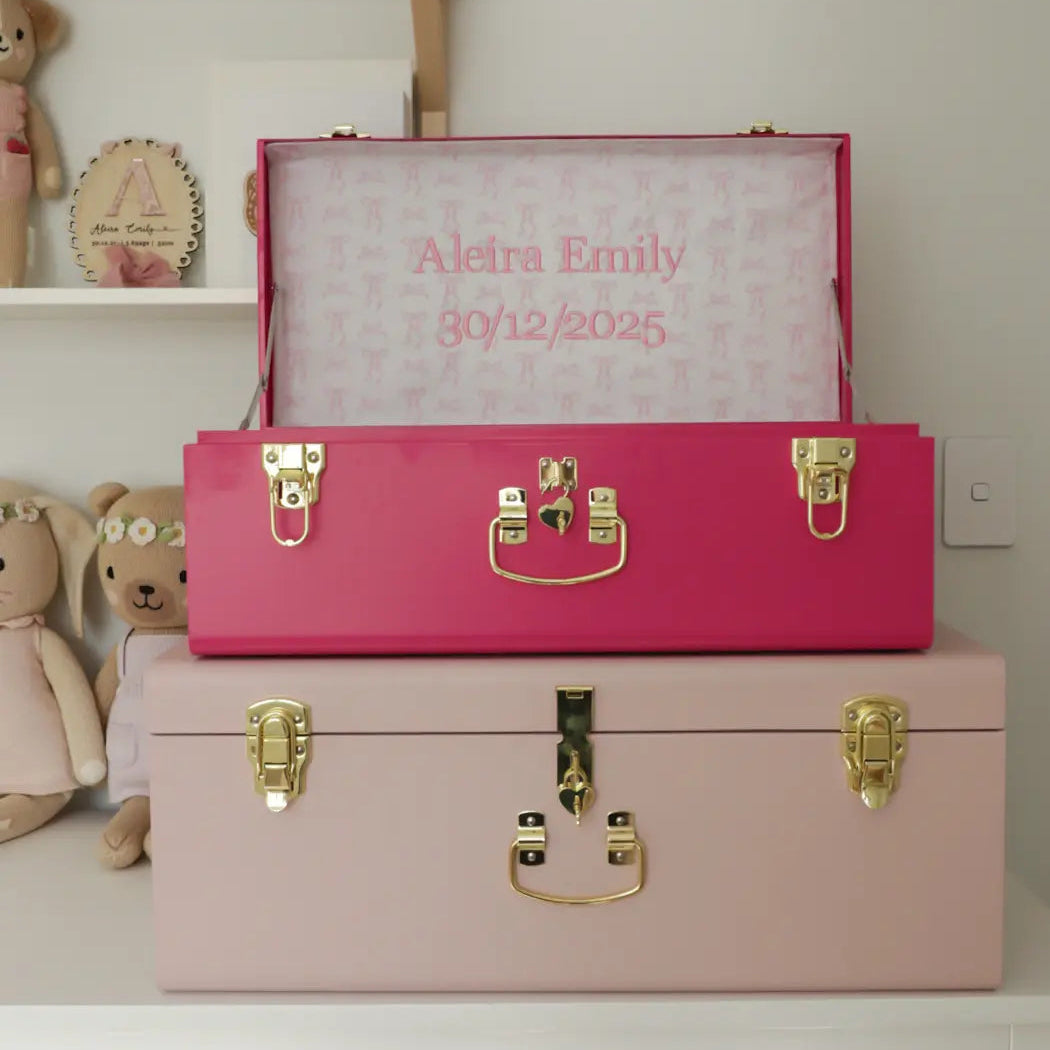 Pink and gold baby memory box with 'Aleira Emily' and date on a white shelf.