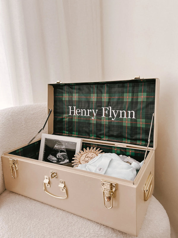 Beige trunk with plaid interior labeled 'Henry Flynn' containing baby items.