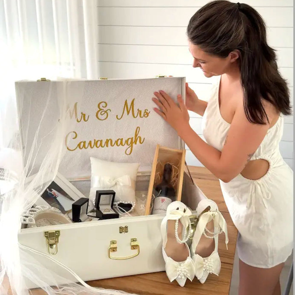 Woman opening a white suitcase with 'Mr & Mrs Cavanagh' on it, containing wedding accessories.