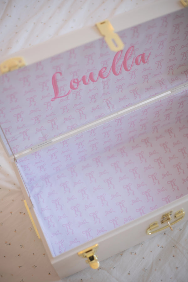 Pink suitcase with 'Louella' printed on it, featuring gold accents.