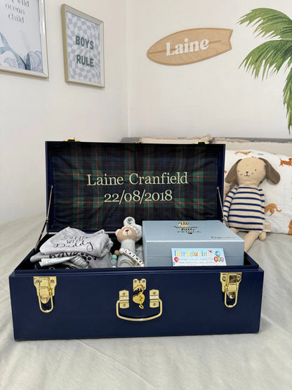 Navy blue gift box with baby items and personalized name on a light gray surface.